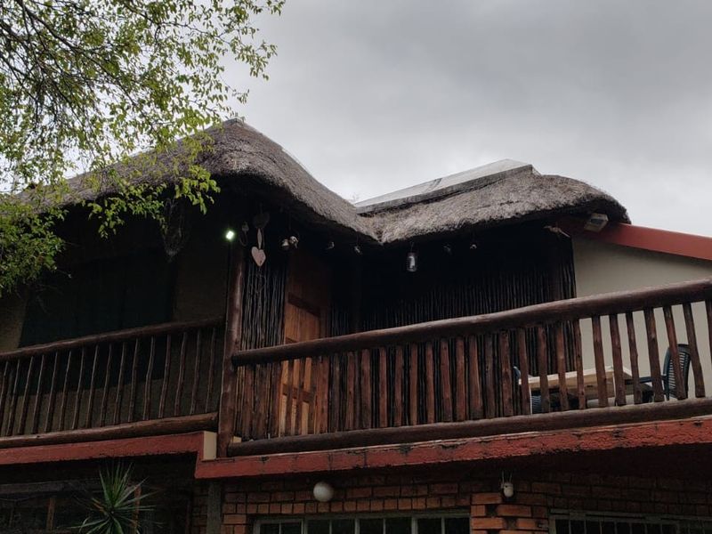 An elevated balcony featuring a traditional thatch roof and rustic wooden railings, set against a brick exterior wall.