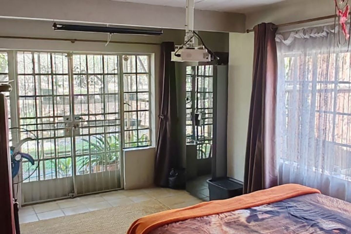 Bedroom featuring tiled flooring, exposed beam ceiling, ceiling fan, and direct access to the garden through a security gate.