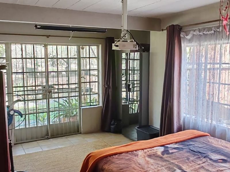 Bedroom featuring tiled flooring, exposed beam ceiling, ceiling fan, and direct access to the garden through a security gate.