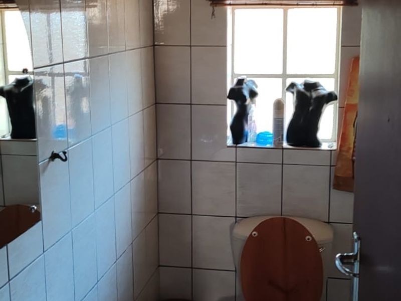 A compact bathroom featuring white wall tiles, a pedestal washbasin, a toilet, and a timber ceiling.