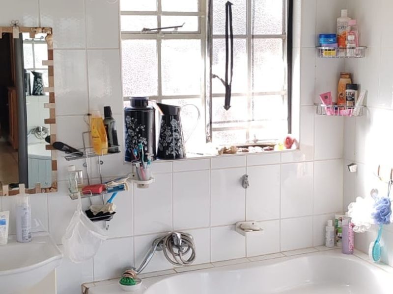 A bathroom featuring a corner bathtub, wall-mounted basin, and tiled finishes. The space requires maintenance to address damaged tiling and worn fixtures.