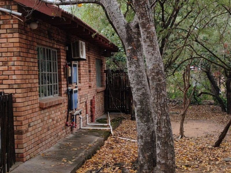 Rear exterior view of a brick house featuring a concrete pathway, security bars on windows, and an installed air conditioning unit.
