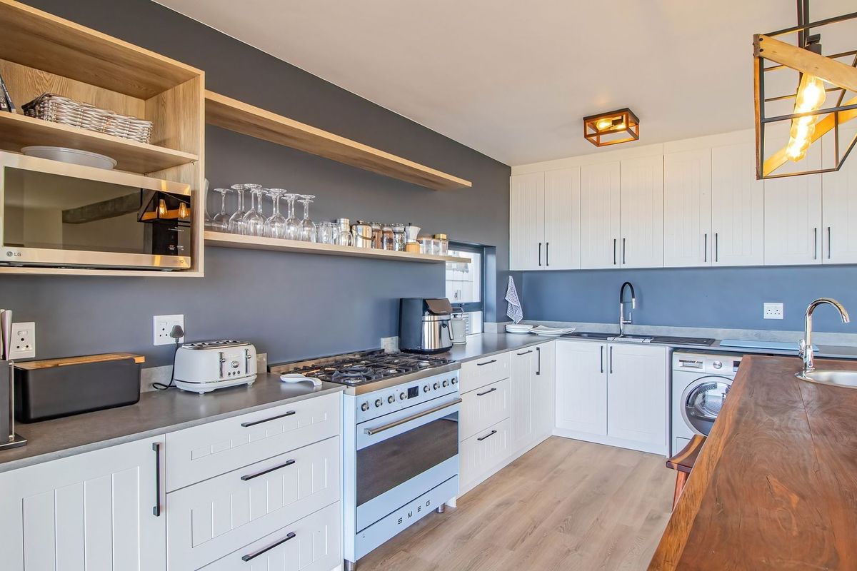 Modern kitchen featuring shaker-style cabinetry, gas stove, integrated appliances, wooden countertops, and floating shelves, finished with a contemporary dark accent wall.