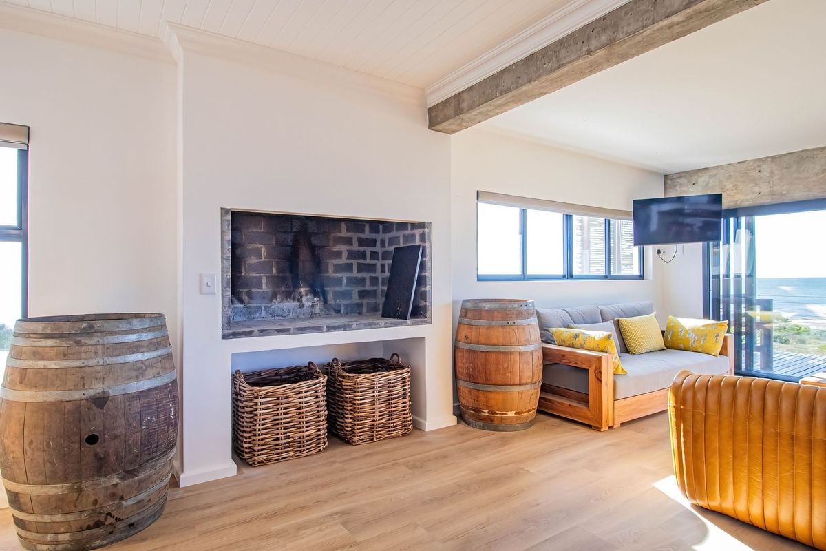 A bright living room featuring a built-in brick fireplace, exposed concrete ceiling beams, and sliding glass doors leading to an outdoor area with ocean views.