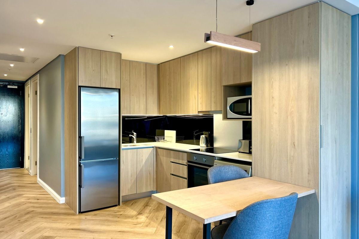 Modern kitchen featuring light wood cabinetry, integrated appliances, stone countertops, and stylish herringbone flooring in an open-plan layout.