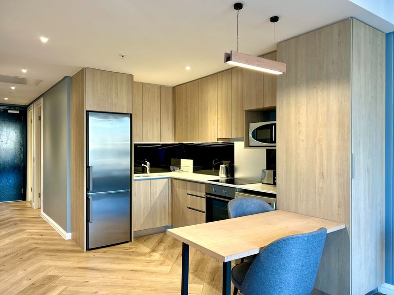 Modern kitchen featuring light wood cabinetry, integrated appliances, stone countertops, and stylish herringbone flooring in an open-plan layout.