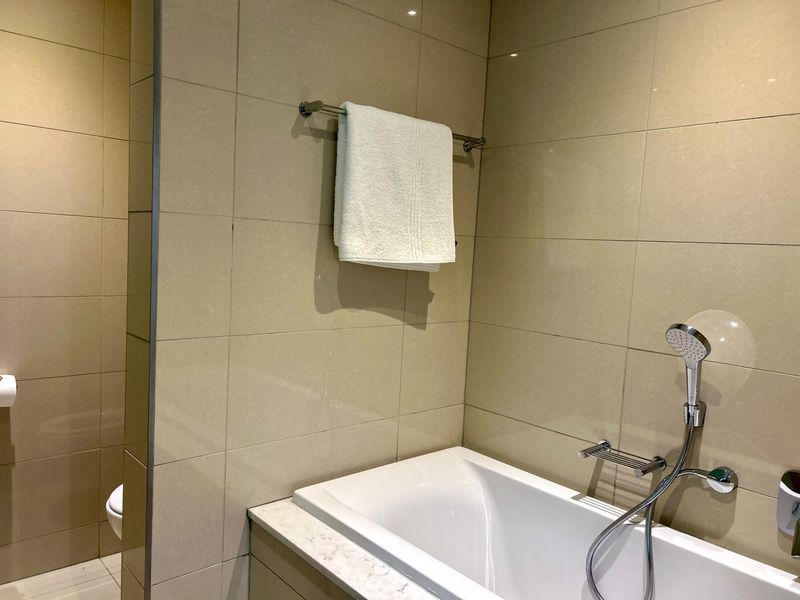 A modern bathroom featuring a built-in bathtub with a handheld shower fixture and neutral wall tiling.