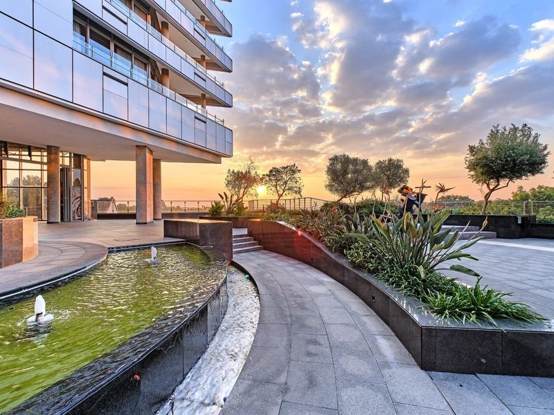 A beautifully landscaped outdoor terrace area featuring a modern water feature, stone paving, and direct access to the apartment building's exterior facade.