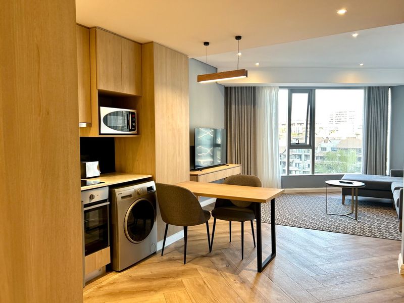 Modern open-plan apartment featuring a sleek kitchen with integrated appliances, herringbone timber flooring, and a bright living area with expansive city views.