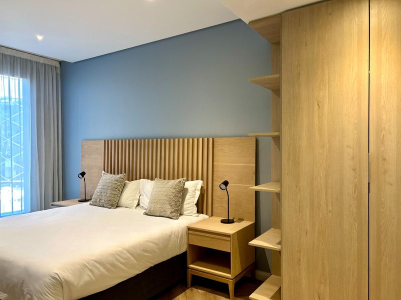 Modern bedroom featuring a custom slatted timber headboard, integrated bedside tables, and built-in floor-to-ceiling wardrobe with open shelving.