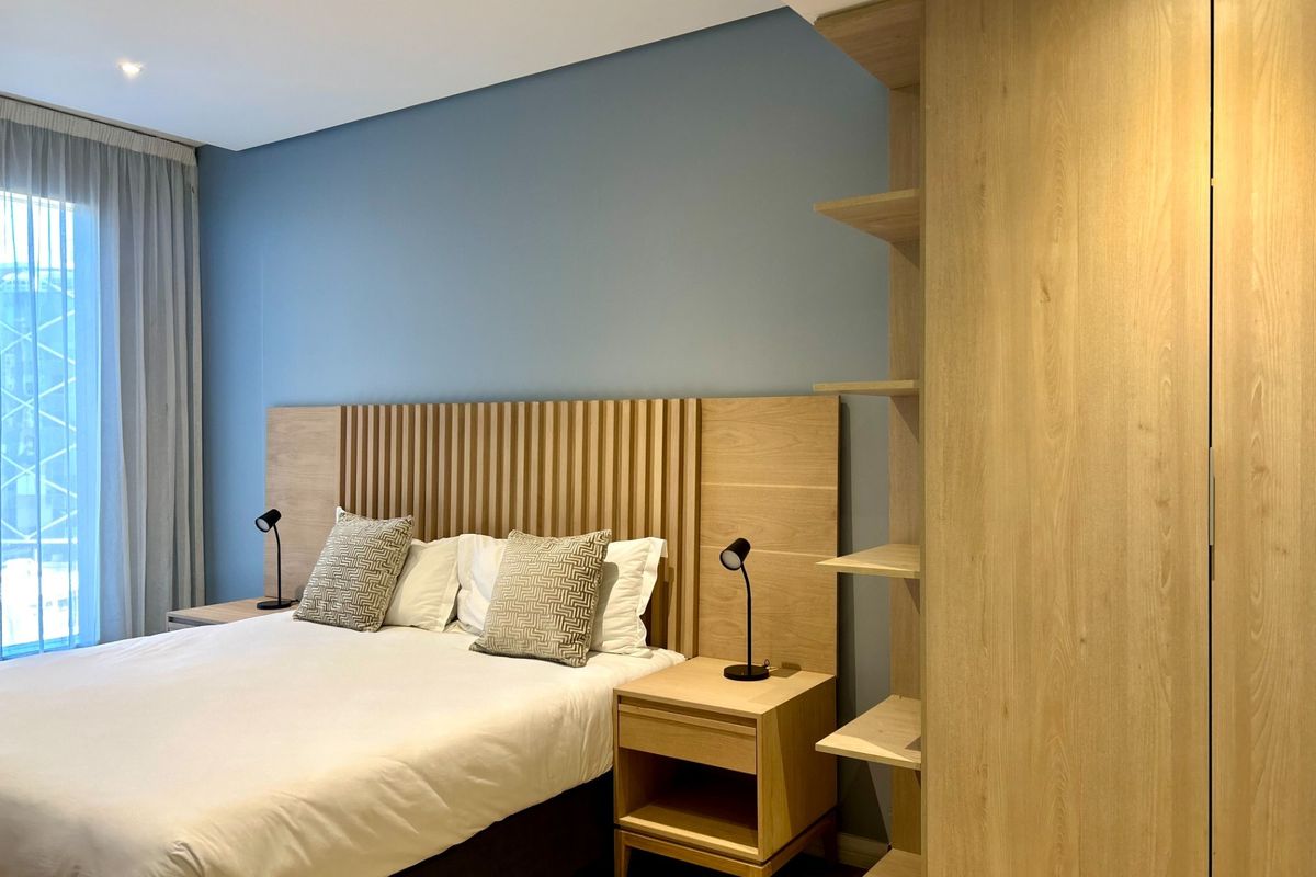 Modern bedroom featuring a custom slatted timber headboard, integrated bedside tables, and built-in floor-to-ceiling wardrobe with open shelving.