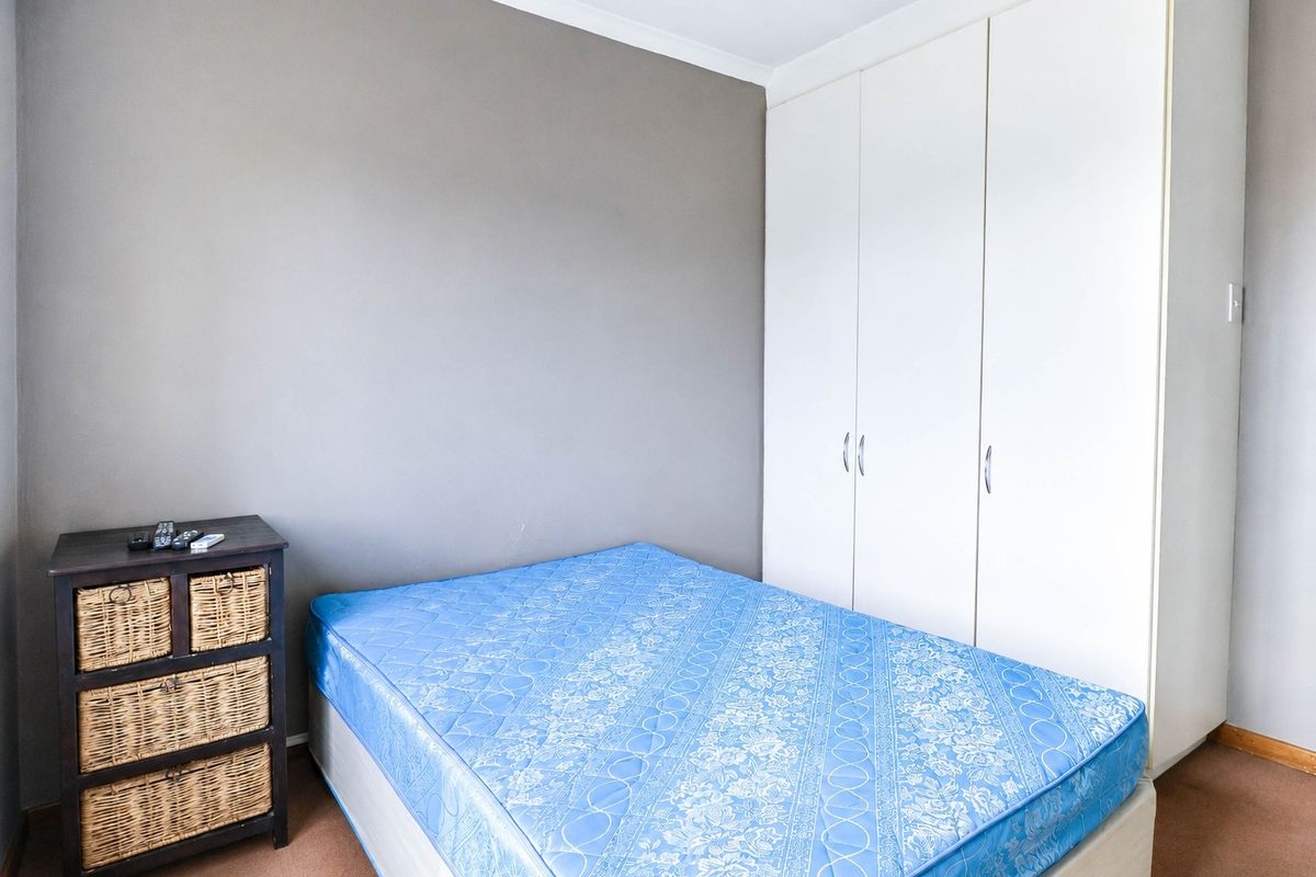 A bedroom featuring neutral wall tones, carpeted flooring, and a white built-in wardrobe providing ample storage space.