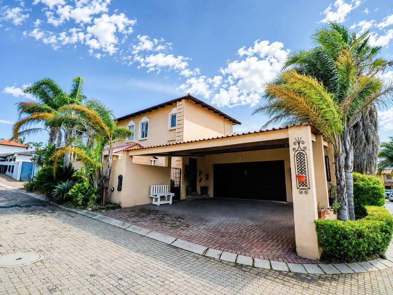 Front exterior view of a two-story house featuring a paved driveway, integrated carport, and tiled roof with established palm trees.