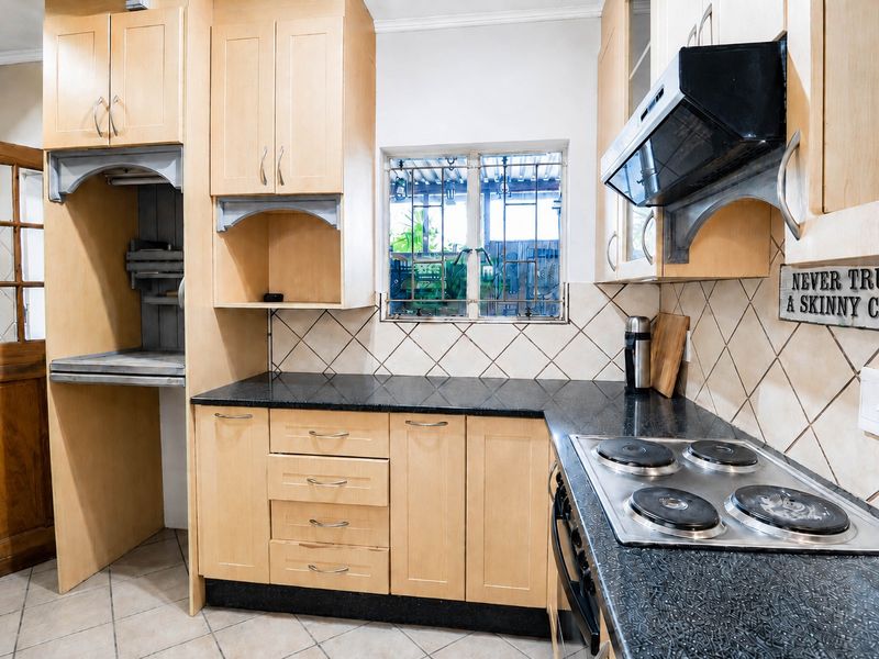 A functional kitchen featuring light wood cabinetry, black granite countertops, an electric hob, and a tiled backsplash with a window view.