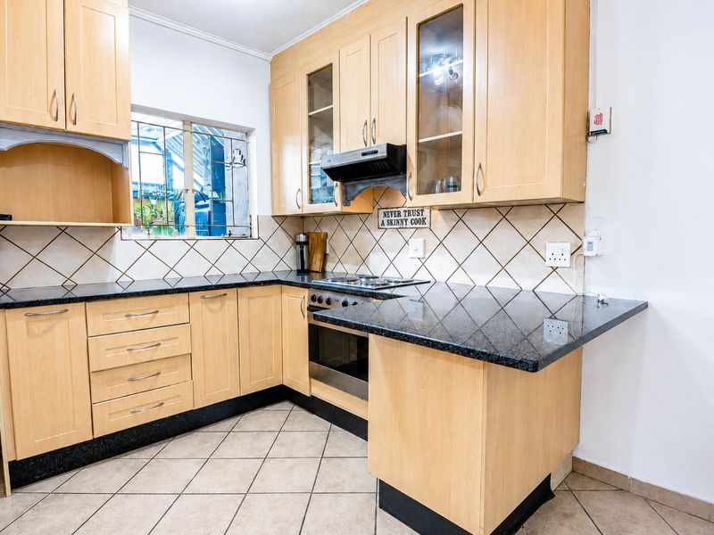 A functional kitchen featuring light wood cabinetry, dark granite countertops, a built-in oven and hob, and tiled flooring with a neutral backsplash.