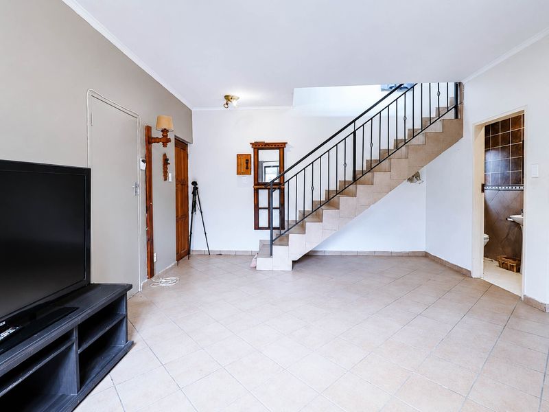 Spacious living area featuring tiled flooring and a central staircase with a metal balustrade, leading to an adjacent bathroom.