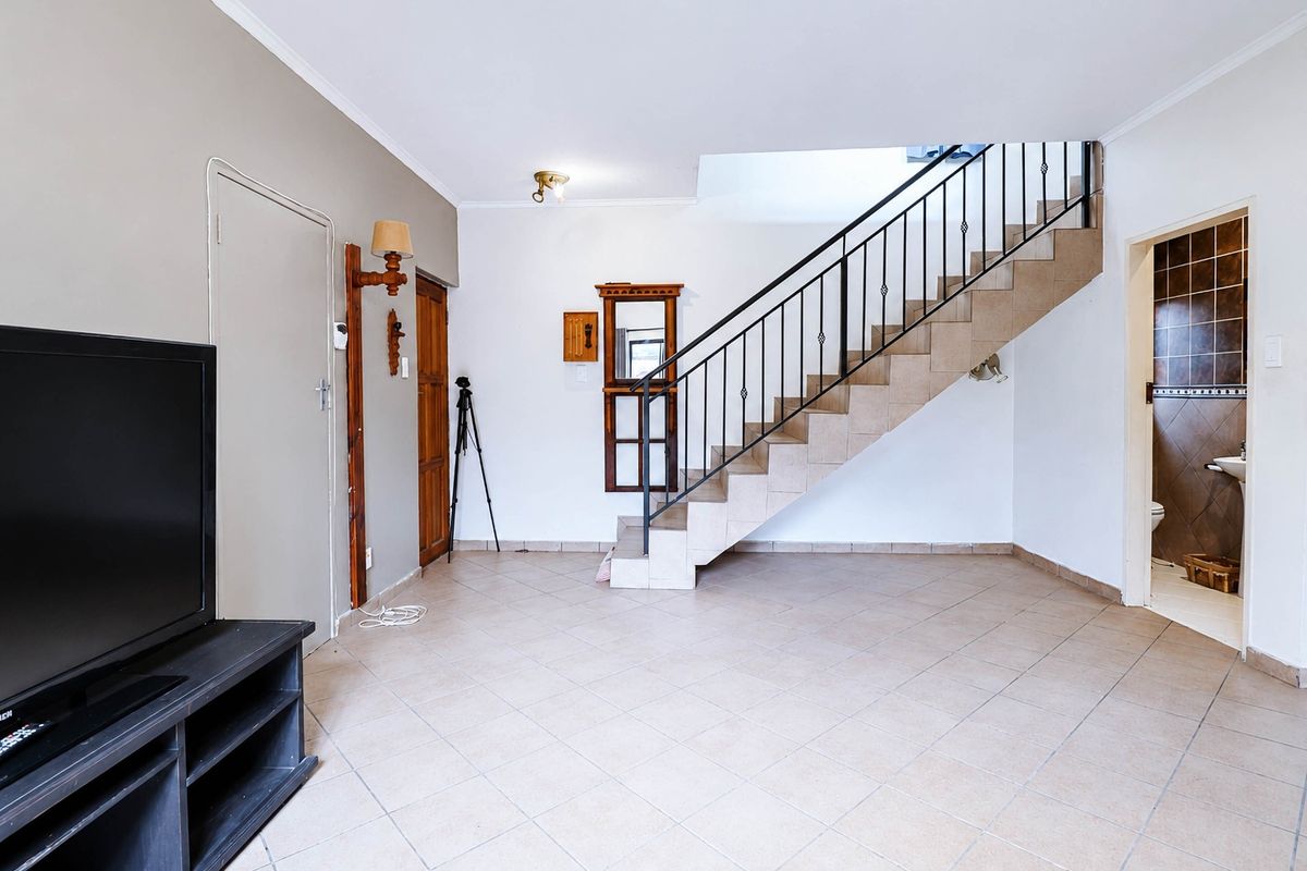 Spacious living area featuring tiled flooring and a central staircase with a metal balustrade, leading to an adjacent bathroom.