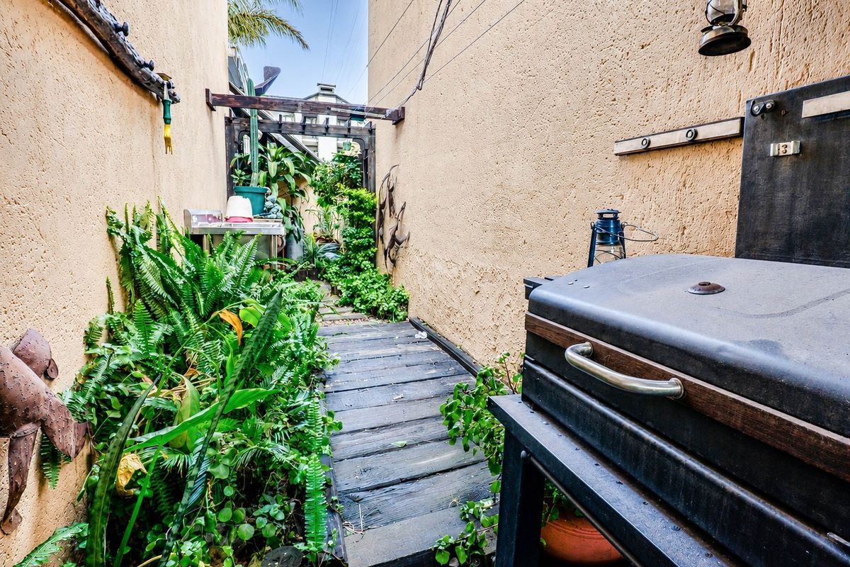 A narrow rear outdoor walkway featuring timber decking, textured walls, and a pergola structure, providing a functional side passage or courtyard area.