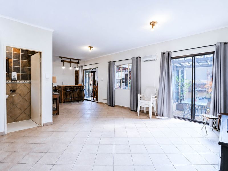 Spacious open-plan living area featuring tiled flooring, a built-in bar, split-system air conditioning, and sliding glass doors leading to an outdoor patio.