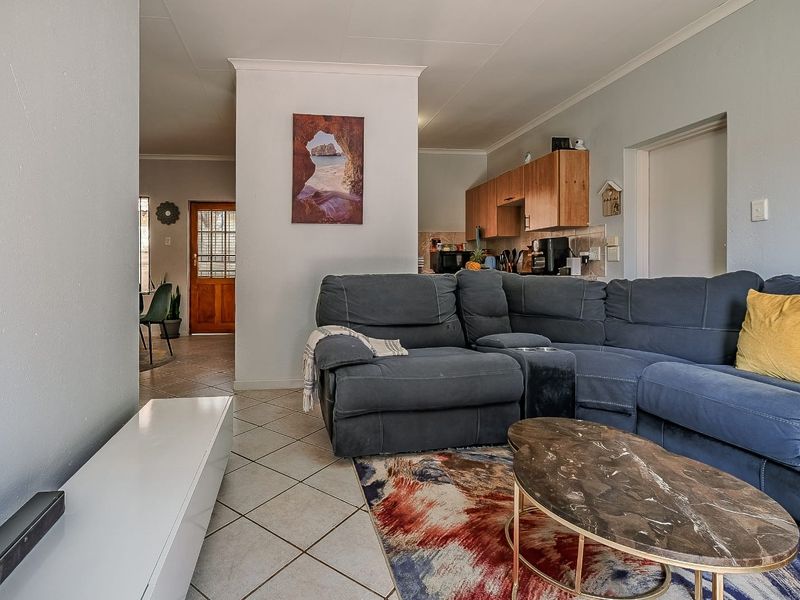 Open-plan living area featuring tiled flooring and a connected kitchen space with wooden cabinetry, providing a functional and integrated layout.