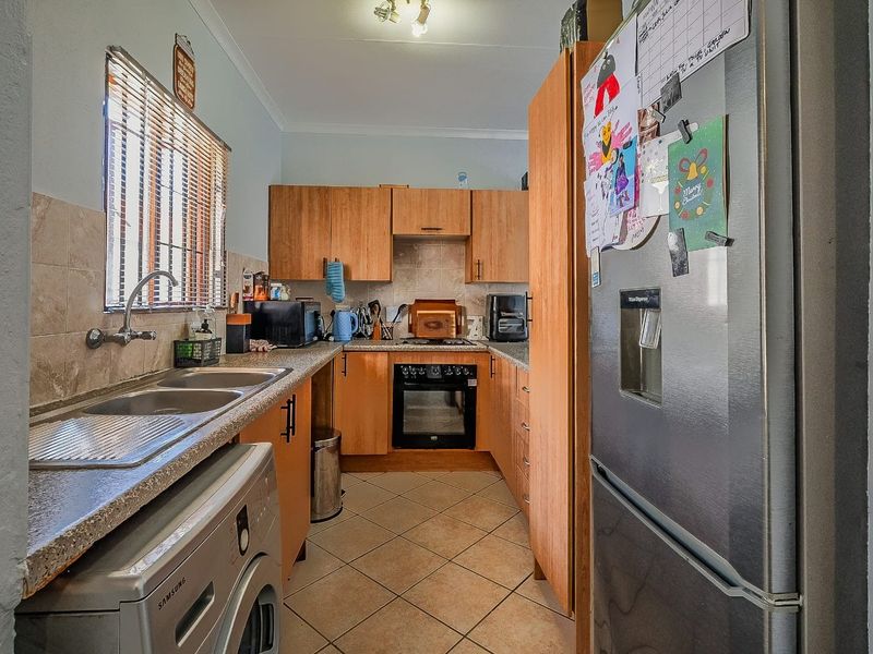 Functional kitchen featuring wooden cabinetry, tiled backsplash, built-in oven, hob, and double sink with tiled flooring.