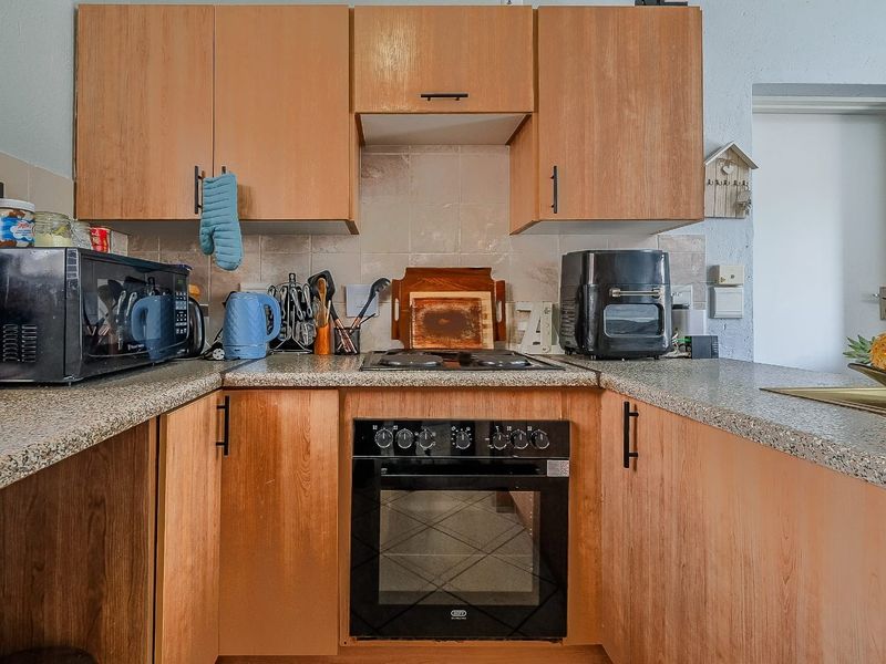A functional kitchen featuring wood-look cabinetry, granite-style laminate countertops, a built-in oven, and an electric hob with a tiled backsplash.
