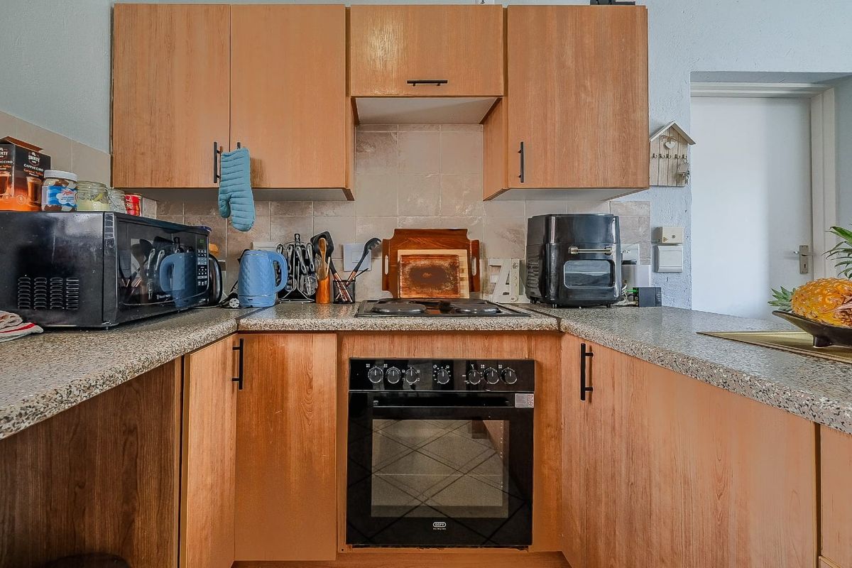 A functional kitchen featuring wood-look cabinetry, granite-style laminate countertops, a built-in oven, and an electric hob with a tiled backsplash.