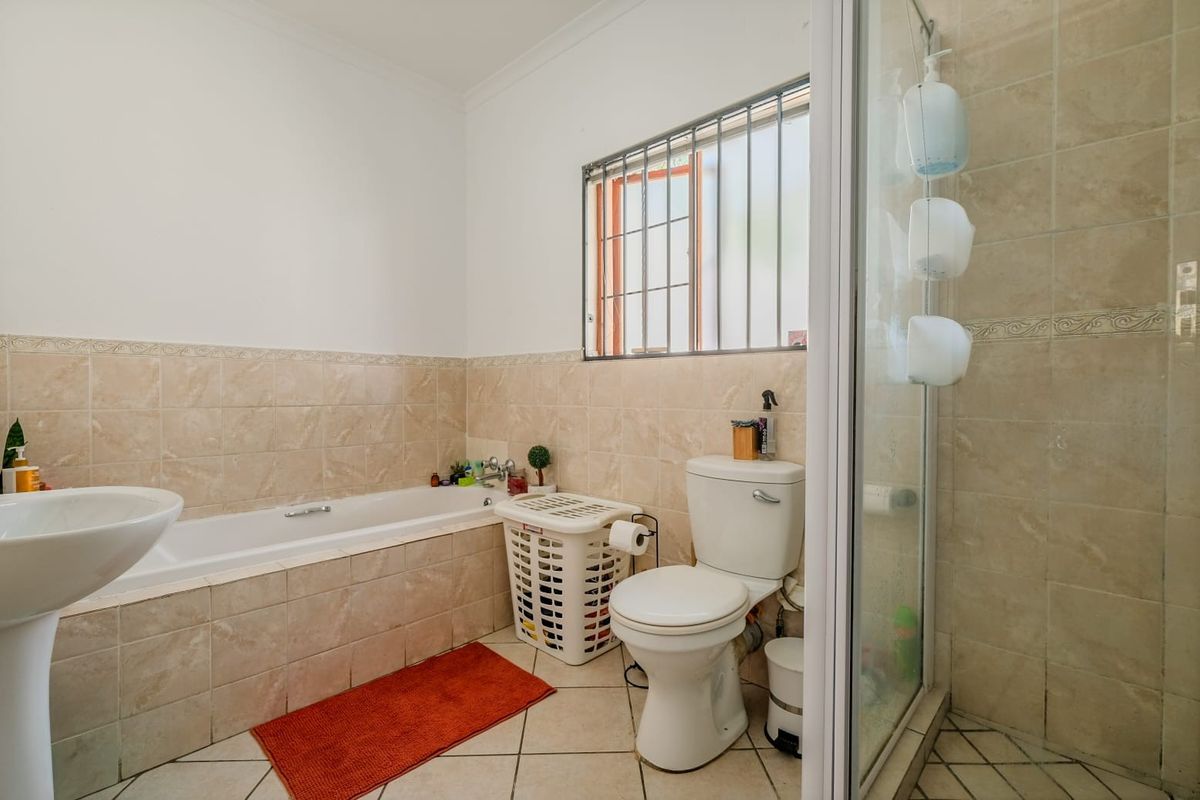 A functional bathroom featuring a built-in bathtub, separate shower enclosure, pedestal sink, and neutral ceramic tiling throughout.