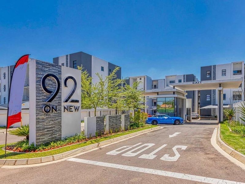 The main entrance and security gatehouse of the 92 On New apartment complex, featuring modern stone-clad signage and a paved access road.