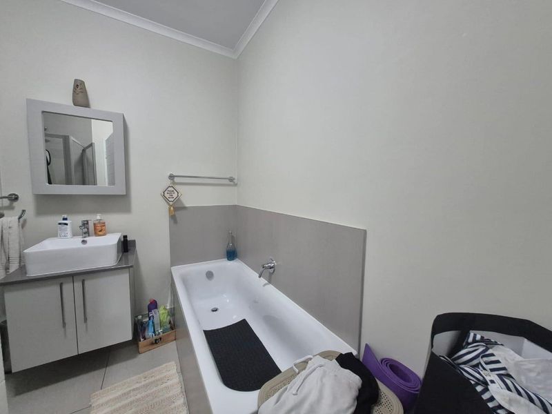 A functional bathroom featuring a modern vanity with basin, wall-mounted mirror, and a bathtub with a tiled splashback.