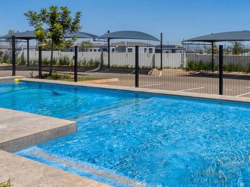 A well-maintained swimming pool area featuring concrete coping, metal perimeter fencing, and adjacent shaded parking bays.