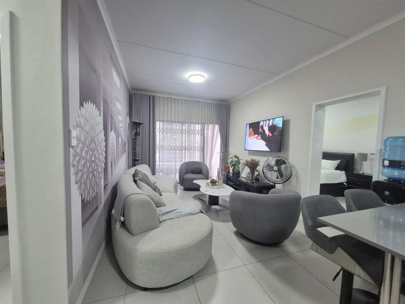 A well-maintained living room featuring tiled flooring, a large sliding glass door for natural light, and a wall-mounted television setup.