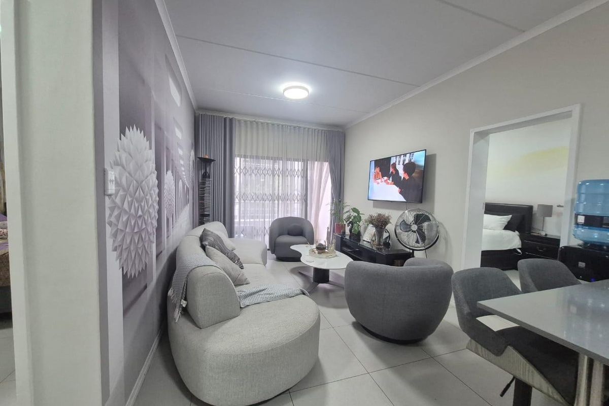 A well-maintained living room featuring tiled flooring, a large sliding glass door for natural light, and a wall-mounted television setup.