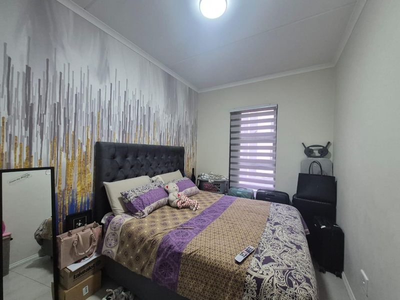 A bedroom featuring tiled flooring, a ceiling light fixture, and modern roller blinds, with a decorative feature wall.