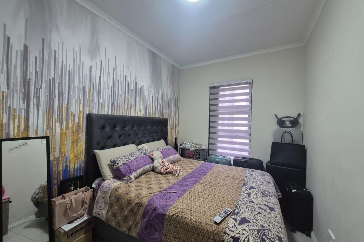 A bedroom featuring tiled flooring, a ceiling light fixture, and modern roller blinds, with a decorative feature wall.