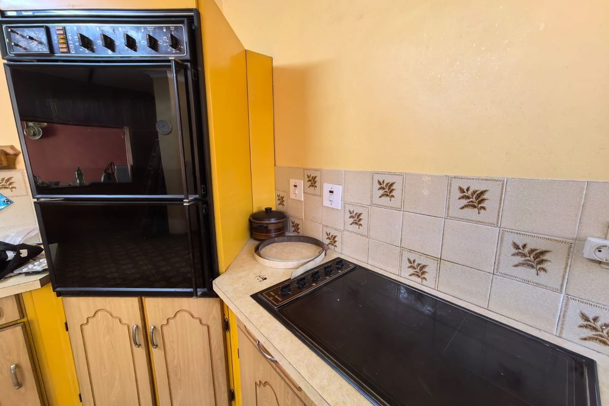A dated kitchen area featuring a built-in oven, electric hob, laminate countertops, and decorative tiled backsplash.
