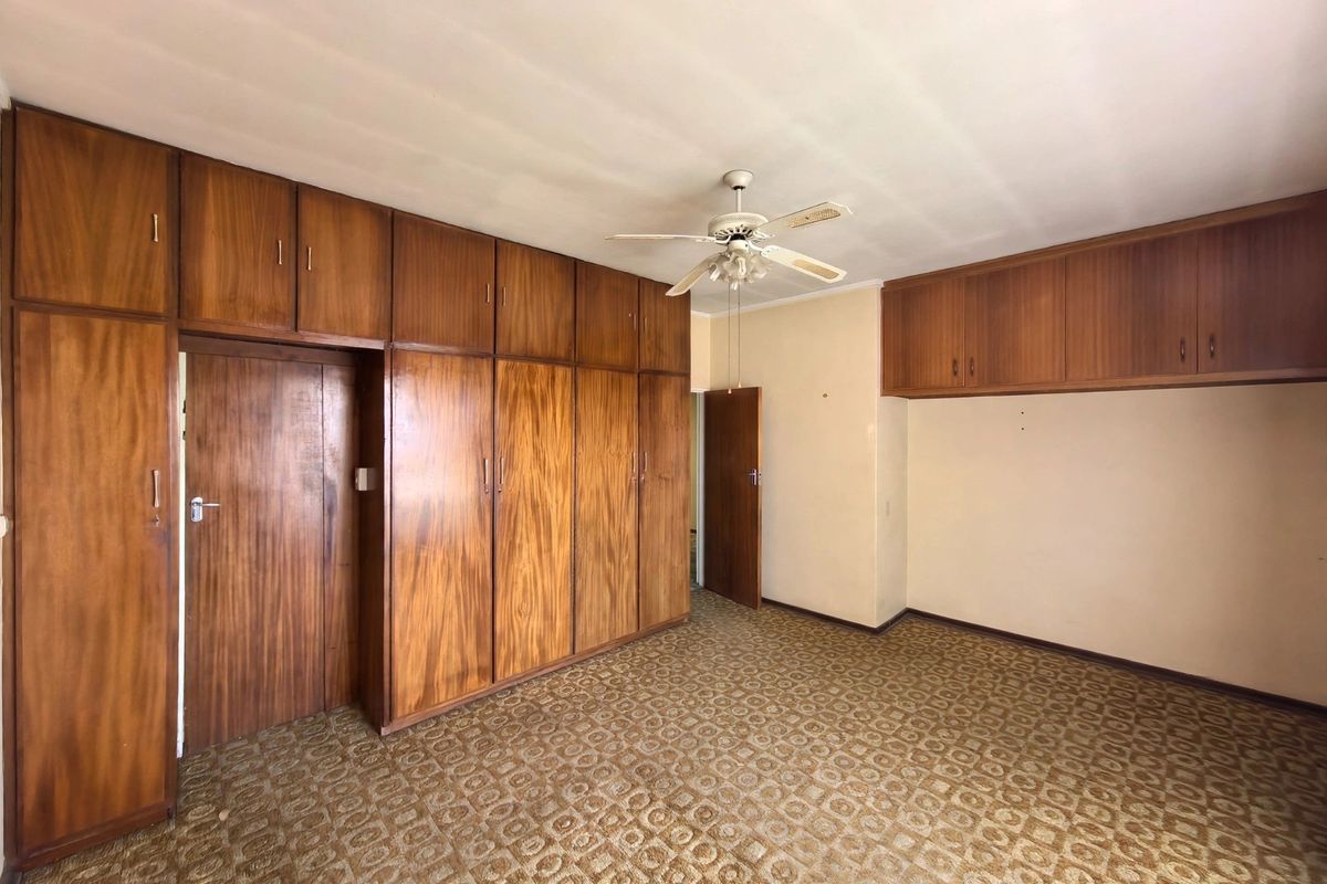 A spacious bedroom featuring extensive built-in wooden cabinetry, a ceiling fan, and carpeted flooring, offering a blank canvas for renovation.