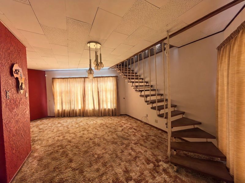 Spacious living area featuring an open-tread staircase, textured feature wall, and acoustic ceiling tiles, offering a blank canvas for renovation.