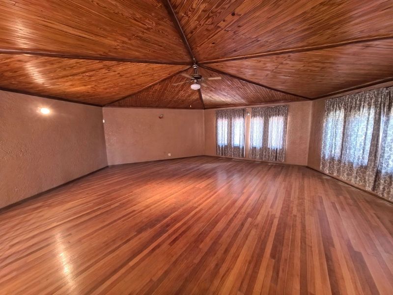 Spacious living area featuring a vaulted timber ceiling, polished hardwood flooring, and a central ceiling fan, offering a warm and inviting atmosphere.