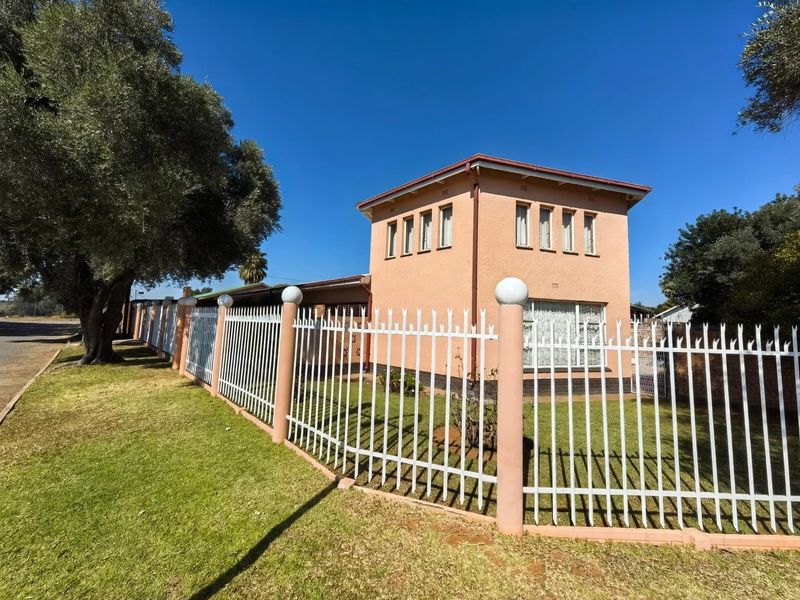 Front exterior view of a two-story house featuring stucco walls, a tiled roof, and secure metal perimeter fencing.