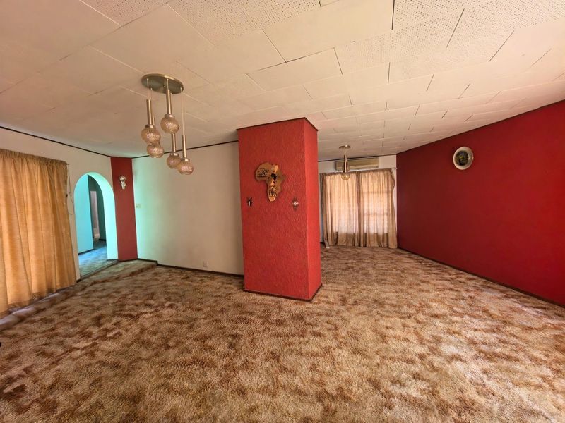 Spacious living area featuring a central structural pillar, acoustic ceiling tiles, and wall-mounted air conditioning, offering a blank canvas for modernization.