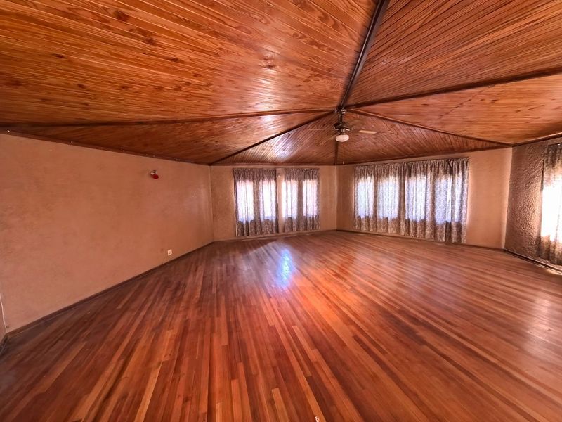 Spacious living area featuring a vaulted timber ceiling, polished hardwood flooring, and large windows that provide ample natural light.