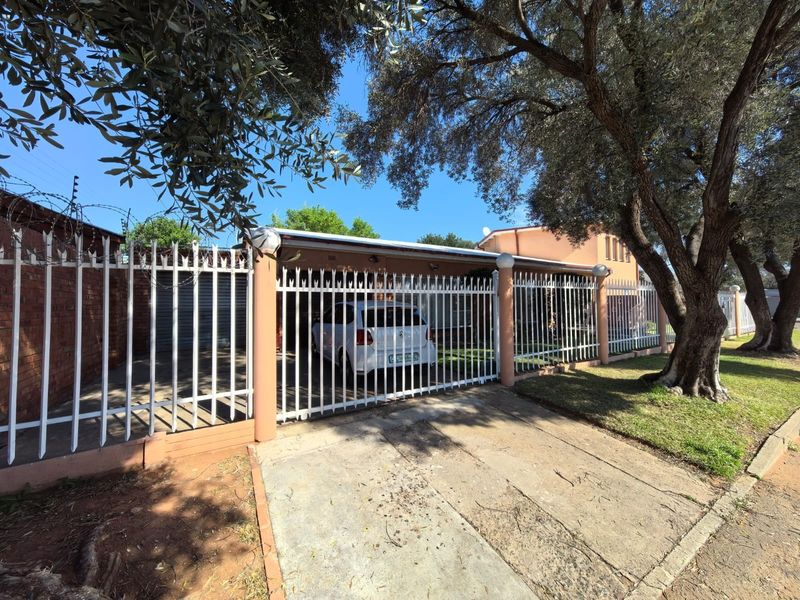 Front view of the property featuring a concrete driveway, covered carport, and secure metal perimeter fencing with integrated electric security wires.