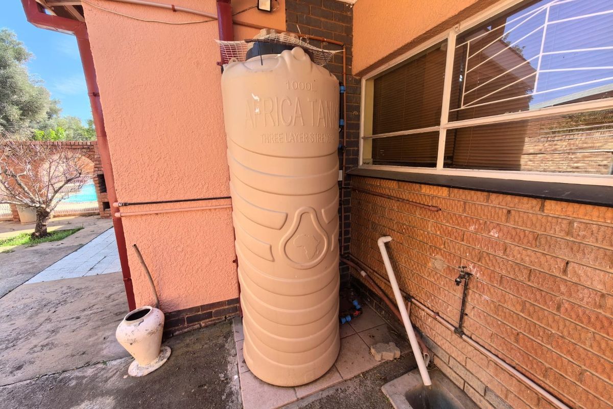 Exterior rear area featuring a 1000L water storage tank installed against a brick and plastered wall with associated plumbing infrastructure.
