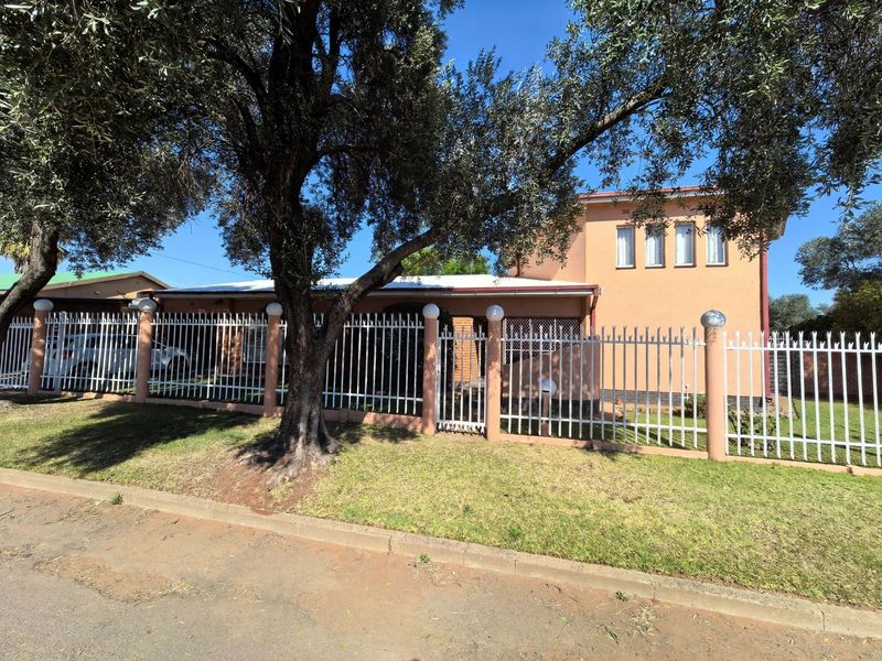 Front view of a residential house featuring a secure metal perimeter fence, concrete pillars, and a tiled roof structure.