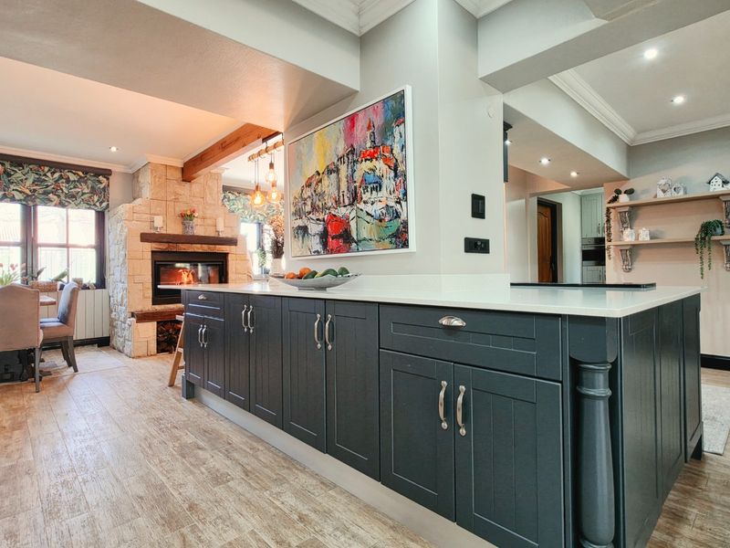 Spacious open-plan kitchen and dining area featuring a large central island, stone fireplace, and modern wood-look tile flooring with integrated lighting.
