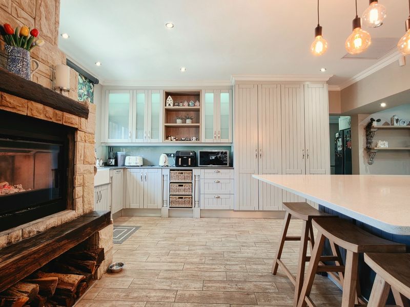 A spacious open-plan kitchen featuring a stone fireplace, custom cabinetry, a large island with quartz countertops, and warm pendant lighting.