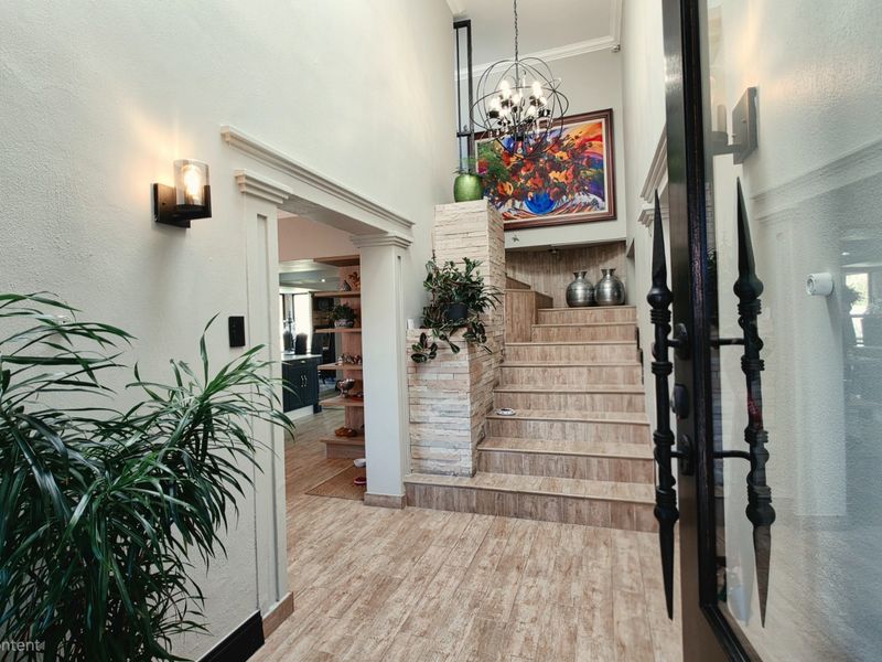 Welcoming entrance hall featuring a grand staircase with stone-clad detailing, elegant chandelier lighting, and durable tiled flooring leading into the main living area.