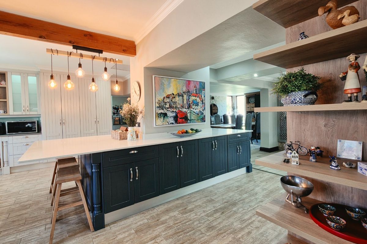 Modern kitchen featuring a large central island with quartz countertops, dark cabinetry, exposed timber beams, and integrated shelving, creating a warm and functional space.