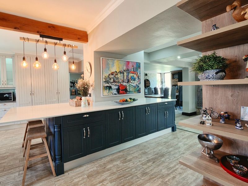 Modern kitchen featuring a large central island with quartz countertops, dark cabinetry, exposed timber beams, and integrated shelving, creating a warm and functional space.